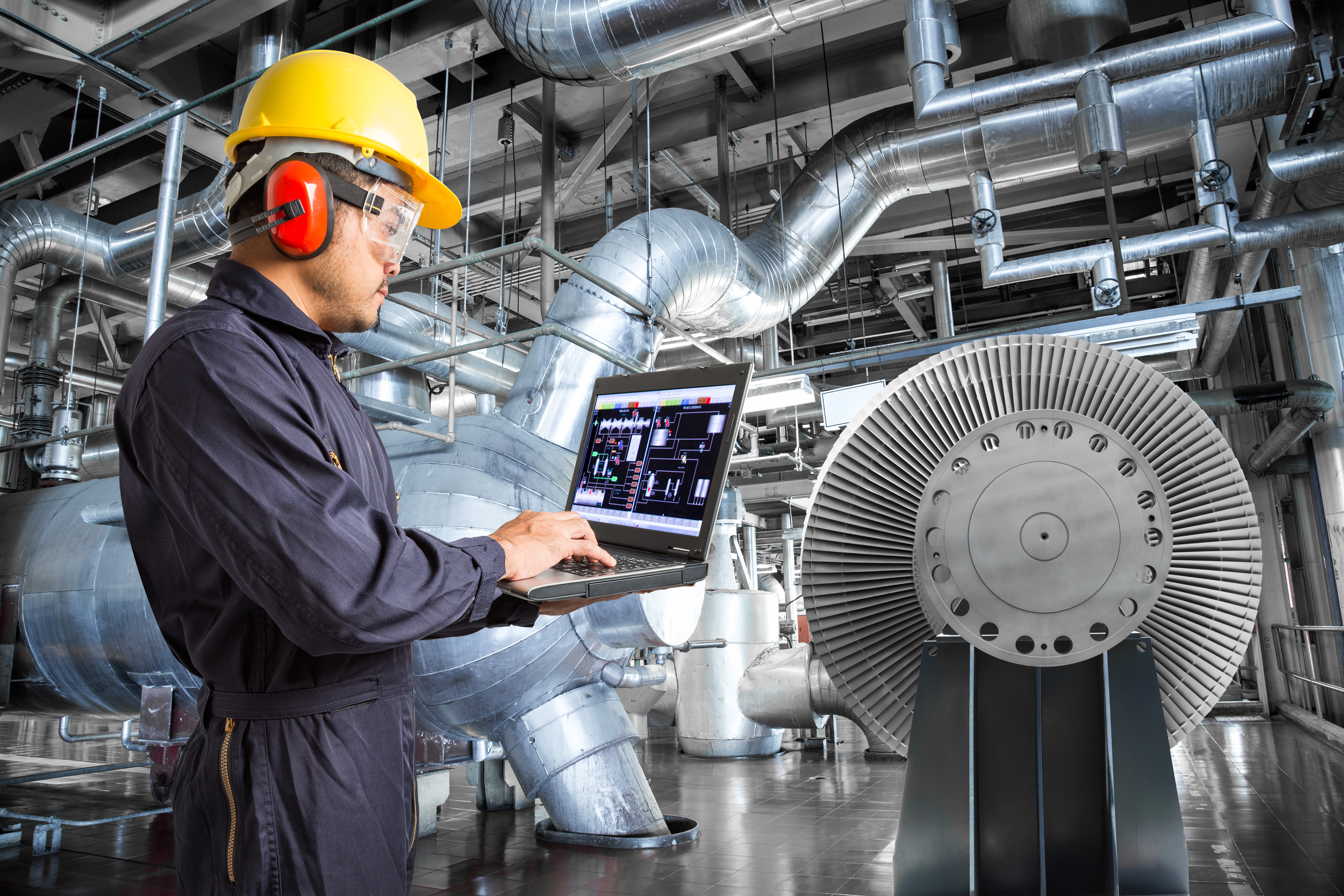 Engineer in protective gear reviewing manufacturing data on a laptop inside an industrial facility